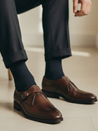 Brown leather shoes with buckles worn with navy socks on a light background